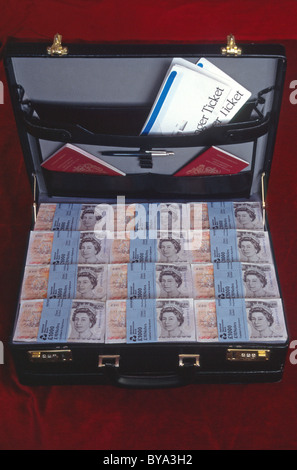Briefcase full of British pound sterling money in cash with travel ticket documents & two UK red burgundy passports concept image money laundering Stock Photo