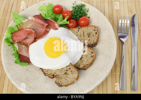 Black Forest smoked ham with a fried egg, bread and cherry tomatoes Stock Photo