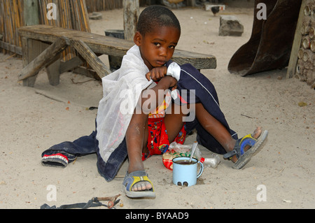 Five-to six-year-old sad boy sitting in front of his meal on the ground in a village near Maun, Botswana, Africa Stock Photo