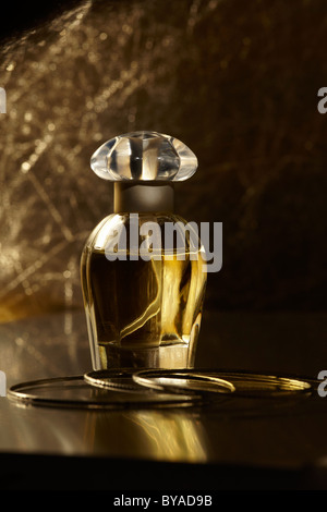 Perfume bottle on a mirrored surface, with gold bracelets Stock Photo