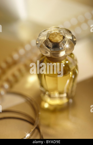 Perfume bottle on a mirrored surface, with bracelets and a pearl necklace, gold coloured Stock Photo
