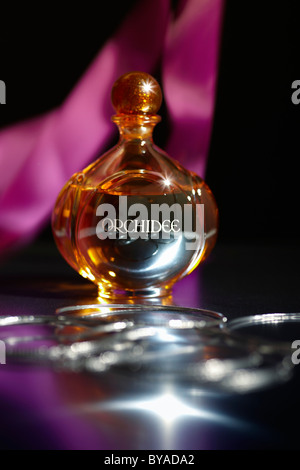Perfume bottle on a mirrored surface, with bracelets and a pink ribbon Stock Photo