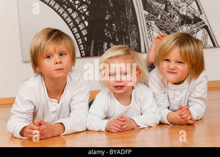 2 boys, 7 and 4 years, and a girl, 1.5 years, lying on the floor Stock Photo