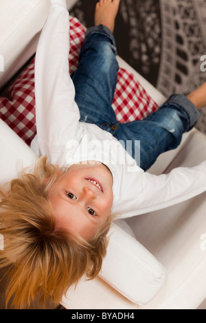 Boy, 4 years, hanging upside down from a white armchair Stock Photo