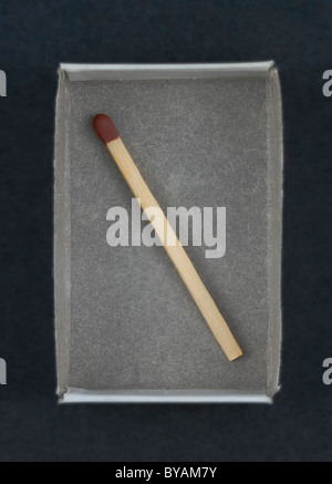 A single brown-tipped safety match inside an open matchbox; on black. Stock Photo