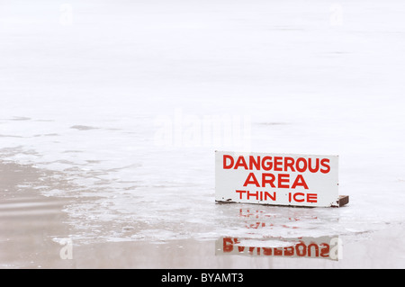 A pond covered in a thin layer of ice with some open water, and a sign signifying the danger. Stock Photo