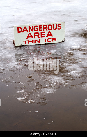 A pond covered in a thin layer of ice with some open water, and a sign signifying the danger. Stock Photo