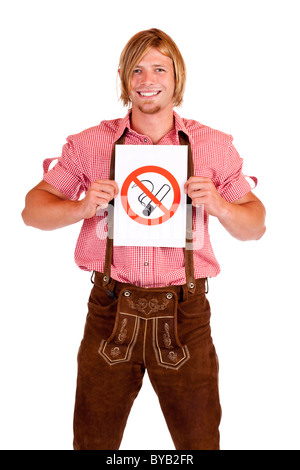 Smiling Bavarian man in lederhose holds non-smoking-rule sign. Isolated on white background. Stock Photo