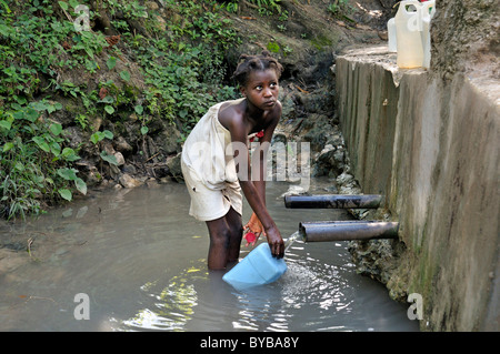Girl filling drinking water from a water source, Petit Goave, Haiti, Caribbean, Central America