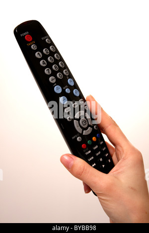 A black remote control for a TV held by a Caucasian female on a white background with a graduated pink in the background Stock Photo