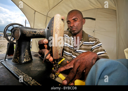 Taylor working on an old mechanical sewing machine, camp for victims of the January 2010 earthquake, Croix-des-Bouquets district Stock Photo