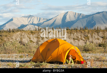 Young woman looking out of an expedition tent, arctic tundra, camping, Mackenzie Mountains behind, Wind River, Yukon Territory Stock Photo