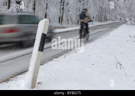 Cyclist being overtaken on a snowy country road in winter, Hesse, Germany, Europe Stock Photo