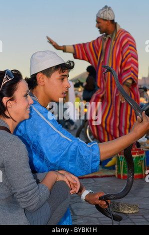 Snake charmer holding black cobra with open mouth with tourist in Place Djemaa el Fna Marrakech Stock Photo