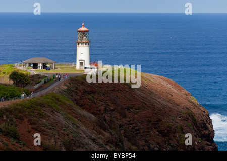 Kilauea Point Lighthouse with tourists. The lighthouse, highlighted by a break in the shore clouds, sits atop a high cliff Stock Photo