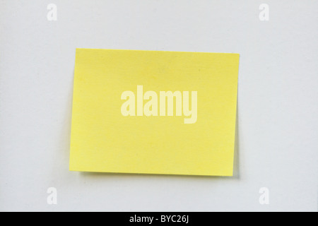 closeup of a small blank yellow sticky note stuck on a white wall Stock Photo