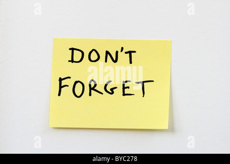 don't forget on a small yellow sticky note stuck on a white wall Stock Photo