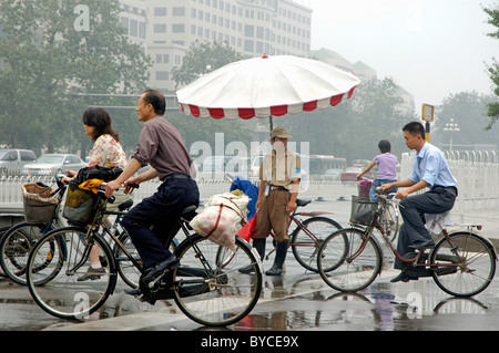 Beijing Traffic warden watching cyclists cycling by in the rain, Beijing, China. Stock Photo