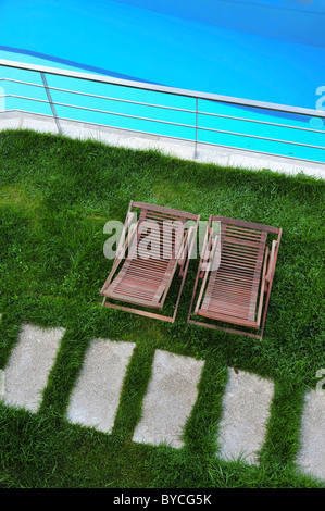 Wood lounge chairs on lawn next to an outdoor swimming pool viewed from above Stock Photo