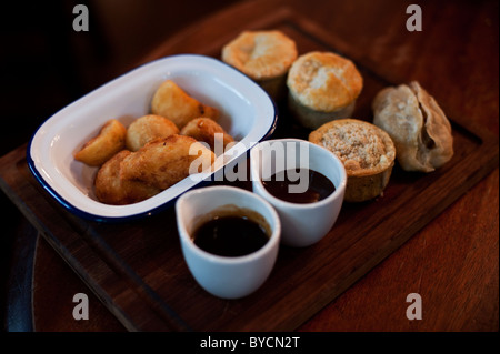 A platter of roasted potatoes and a tasting sample of pies and gravy at a traditional English pub. Stock Photo