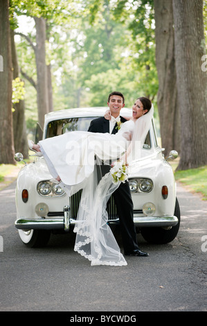 Newly married groom holding his new bride in his arms, laughing as they arrive at their wedding reception. Stock Photo