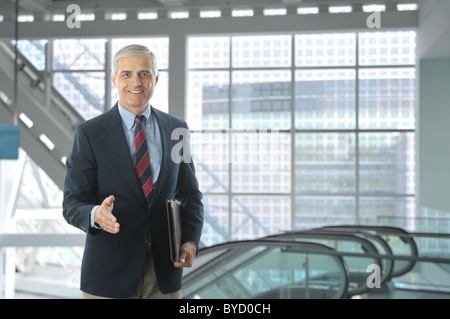 Smiling middle aged businessman standing in the lobby of a modern office building. Man is wearing a blue blazer and khaki pants. Stock Photo