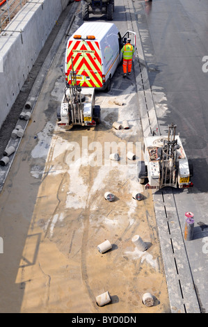 Concrete drilling equipment forming holes in road for crash barrier posts during M25 motorway widening project Stock Photo