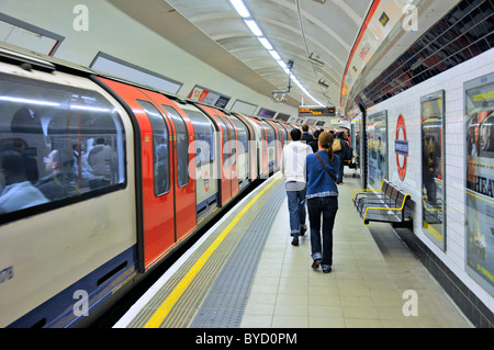 Shepherds Bush underground station with Central Line tube train moving away as passengers walk along platform to exits London England UK Stock Photo