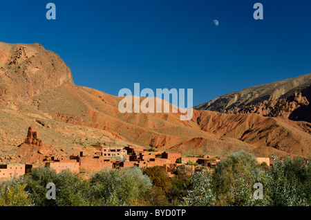Moon in blue sky over red soil and rock formations in Dades Gorge Morocco Stock Photo