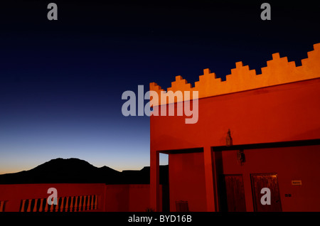 Orange adobe crenelations on rooftop of resort with indigo sunset at twilight in Tinerhir Morocco Stock Photo