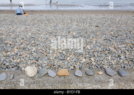 stones and pebbles on a wall at the seaside people in the distance in the sea Stock Photo