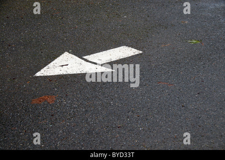 A white arrow painted on asphalt points in one direction. Stock Photo