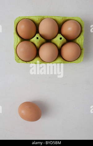 Six brown eggs in an egg carton and one egg beside it Stock Photo