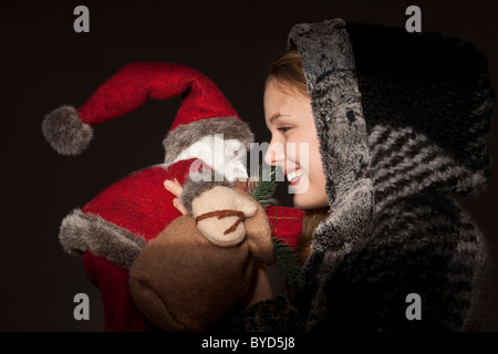 Smiling young woman in a hooded winter jacket Santa claus doll in her arm Stock Photo