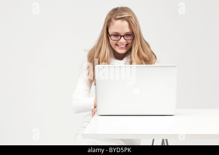 Blonde young woman dressed in white working on a laptop Stock Photo