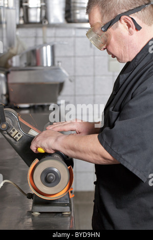 Chef sharpening a knife with a belt grinder in a kitchen Stock Photo
