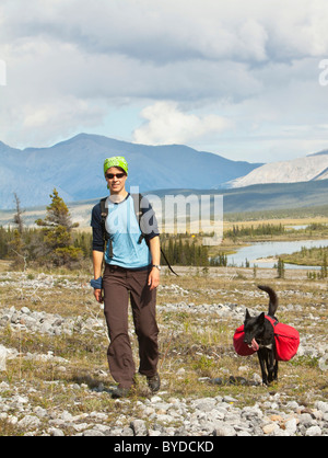 Young woman hiking, pack dog, Alaskan Husky, sled dog, carrying a dog pack, backpack, Wind River and Mackenzie Mountains behind Stock Photo