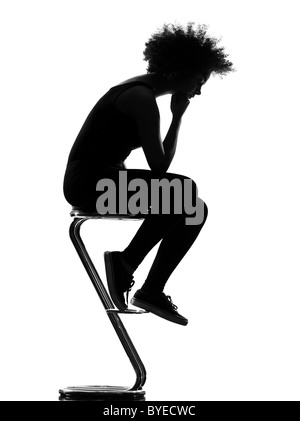 beautiful funny young afro american woman sitting on footstool pensive in silhouette shadow on studio isolated white background Stock Photo