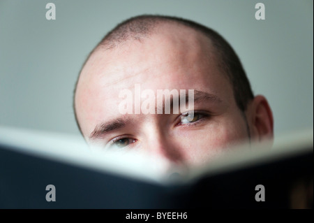 Young man hiding behind a book, looking over the edge of the book Stock Photo