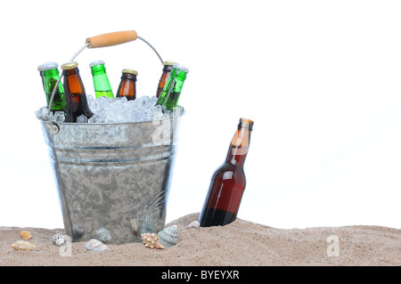 Assorted beer bottles in a bucket of ice in the sand isolated on white. Stock Photo