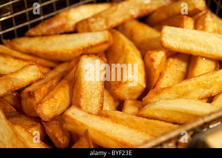 golden brown freshly cooked home made chips made from irish potatoes in a deep fat fryer basket Stock Photo