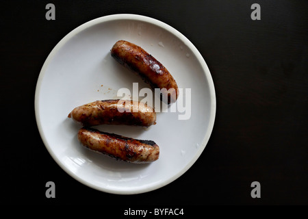 Three perfectly cooked pork sausages on a white dinner plate, ready to be consumed Stock Photo