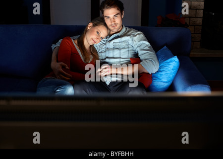 young heterosexual couple hugging on sofa and watching movie on tv at home. Horizontal shape, front view, copy space Stock Photo