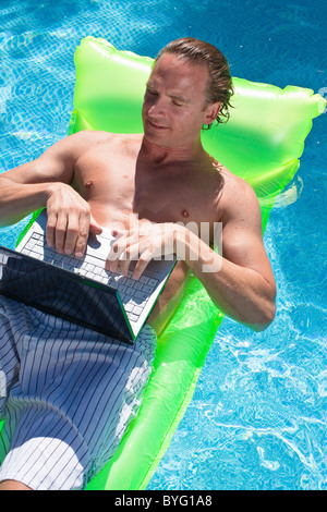 Man floating on inflatable raft and working on laptop Stock Photo