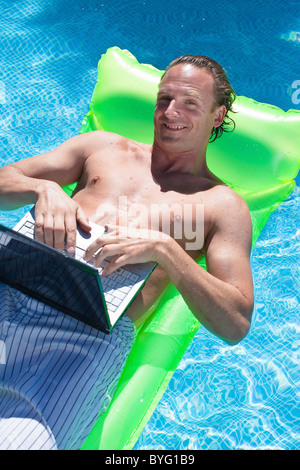 Man floating on inflatable raft and working on laptop Stock Photo