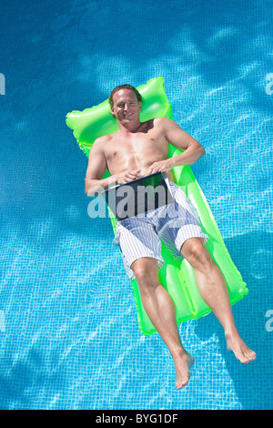 Man floating on inflatable raft and working on laptop Stock Photo