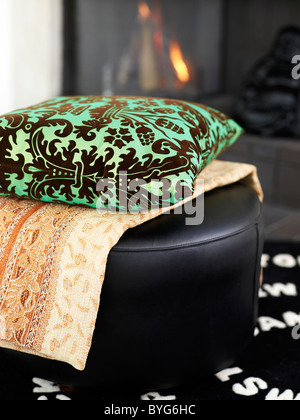 Still-life with ornate cushion and cloth on top of black leather hassock Stock Photo
