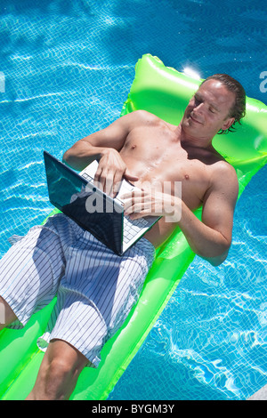 Man floating on inflatable raft and working on laptop Stock Photo