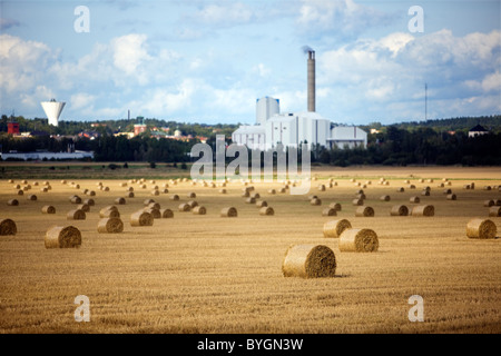 Hay bales in field with factory in distance Stock Photo