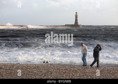 Men walking on Roker beach with a dog in stormy weather, North East England, UK